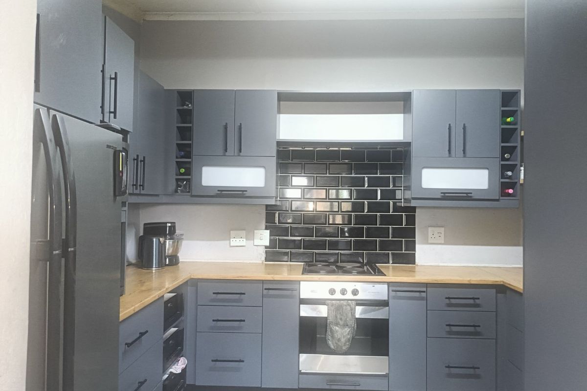 Modern kitchen featuring dark grey cabinetry, wooden countertops, a black subway tile backsplash, and integrated stainless steel oven and hob.