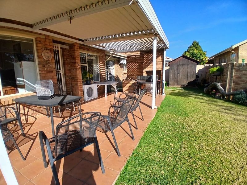 A covered brick patio featuring a built-in braai, tiled flooring, and direct access to a private garden with a storage shed.