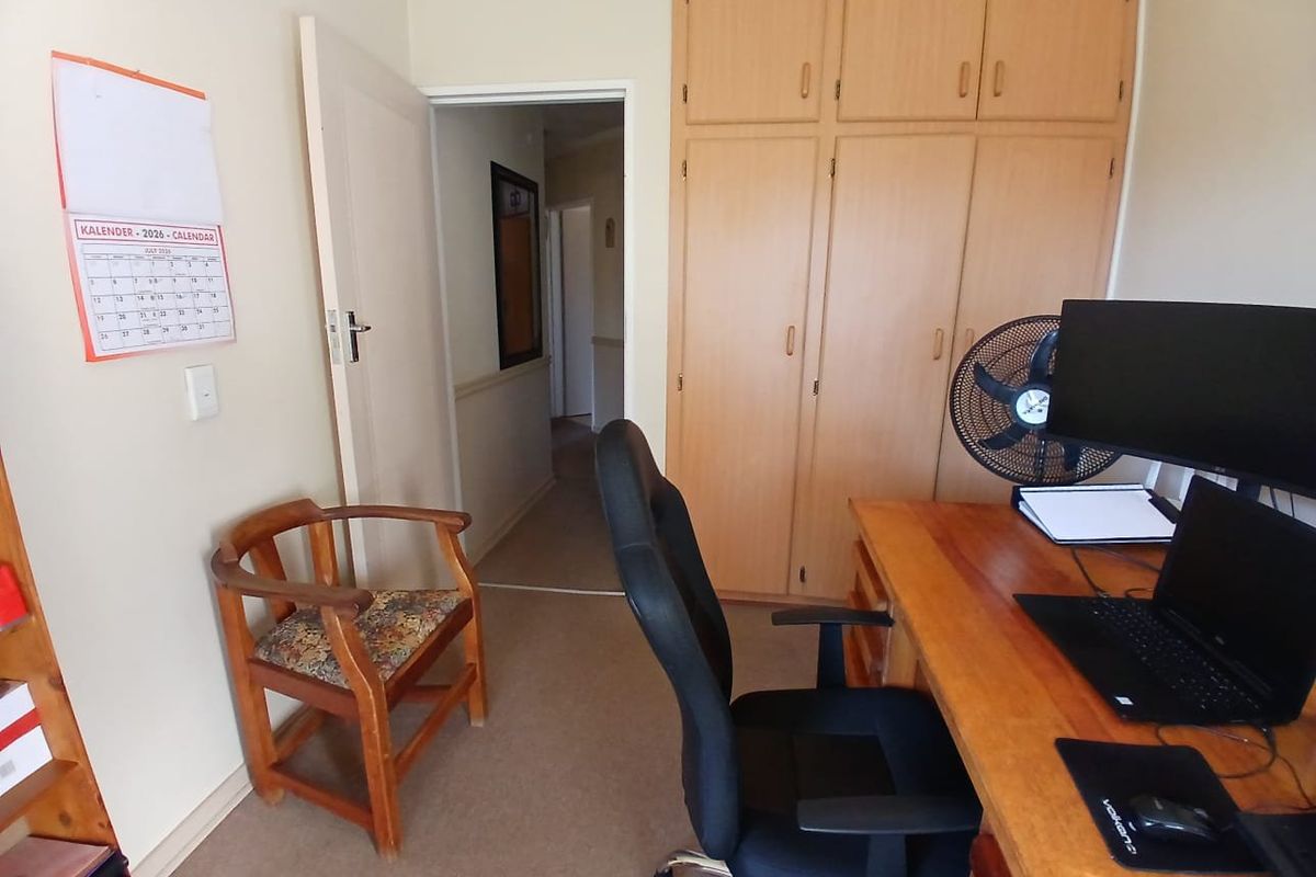 A bedroom featuring built-in wooden cupboards and carpeted flooring, currently utilized as a home office space.