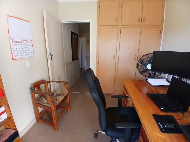 A bedroom featuring built-in wooden cupboards and carpeted flooring, currently utilized as a home office space.