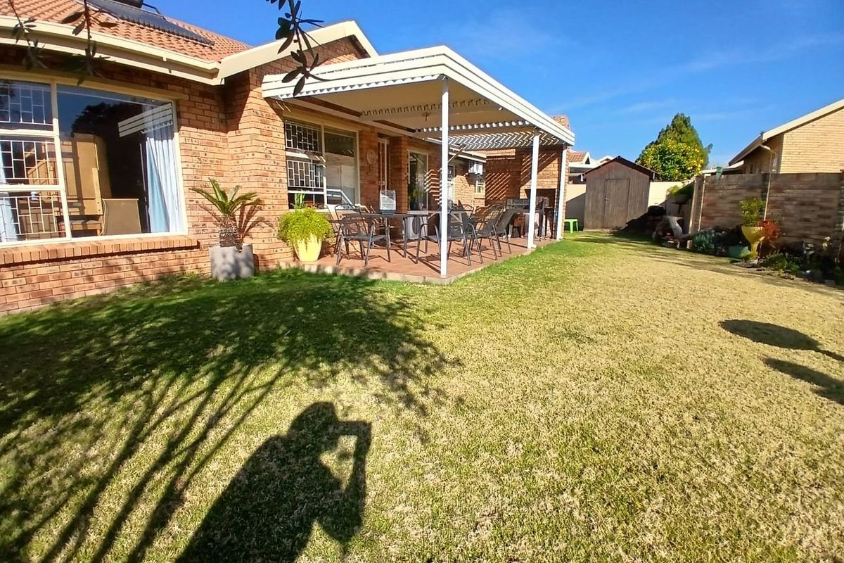Rear view of the townhouse featuring a brick facade, a covered patio area, and a well-maintained lawn with a garden shed.