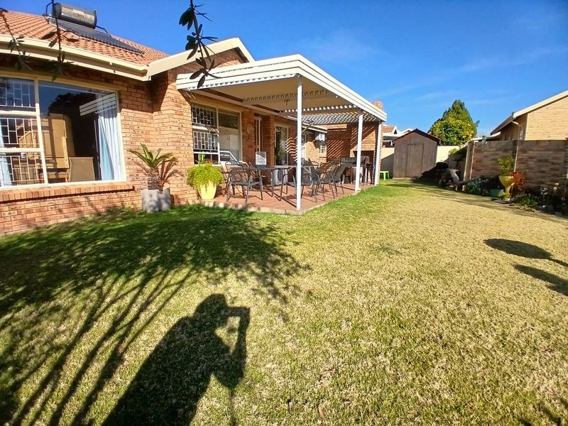 Rear view of the townhouse featuring a brick facade, a covered patio area, and a well-maintained lawn with a garden shed.