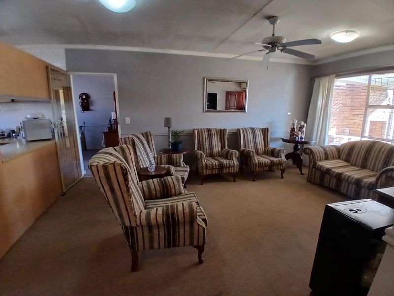 Open plan living area featuring a ceiling fan, carpeted flooring, and integrated kitchen cabinetry, offering a functional layout with potential for modernization.