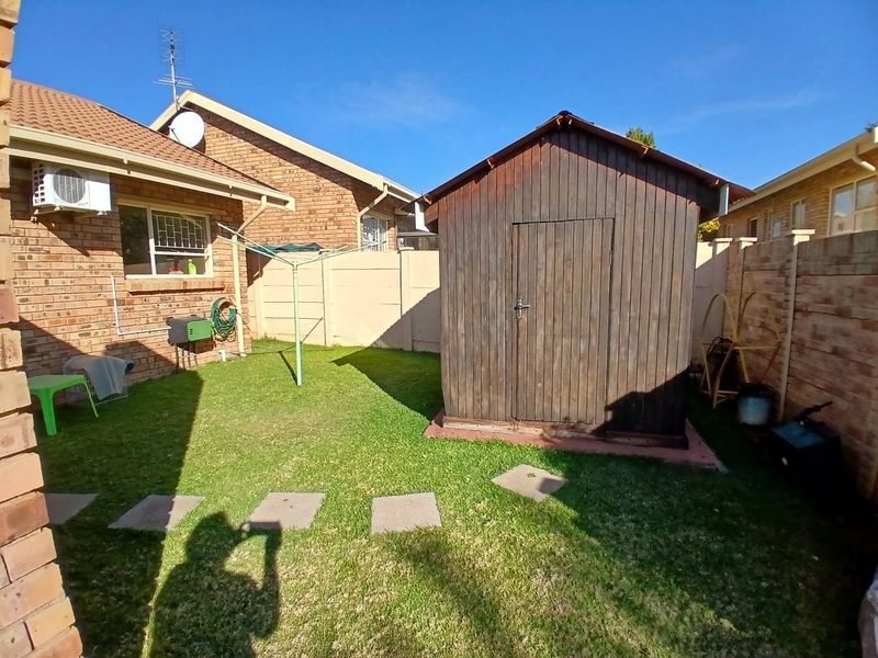 Rear garden area featuring a brick townhouse exterior, a timber storage shed, and a small lawn with paved stepping stones.