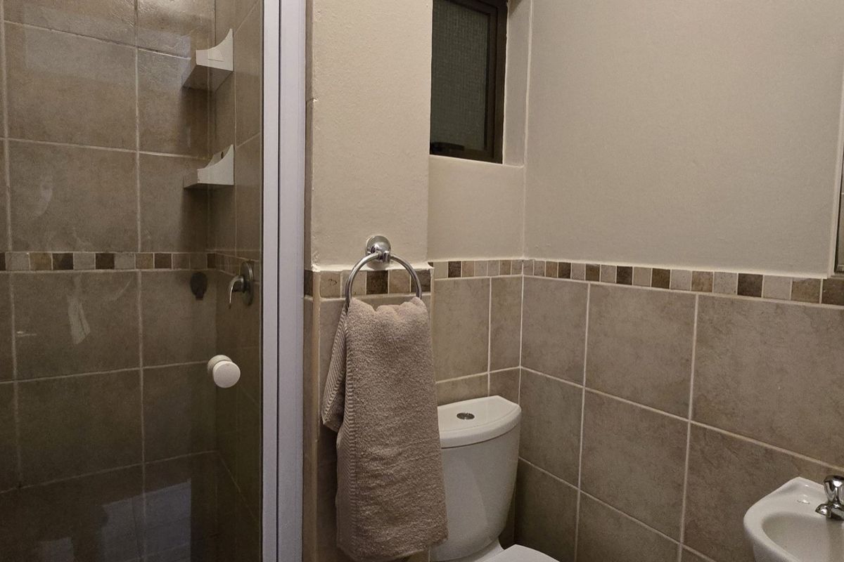 A functional bathroom featuring a shower enclosure, tiled walls with decorative border, a wall-mounted basin, and a medicine cabinet.