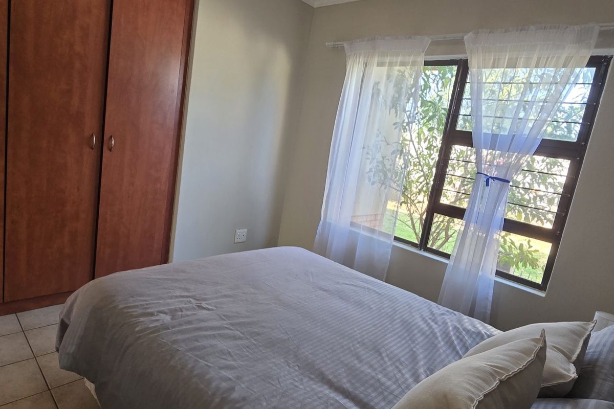A functional bedroom featuring built-in wooden cupboards, tiled flooring, and a window fitted with security bars for added safety.
