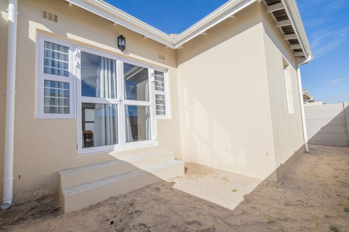 Rear exterior view of the house featuring a double glass door entrance with concrete steps and clean painted wall finishes.