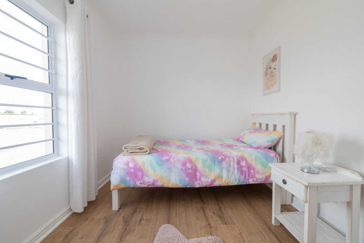 A bright and clean bedroom featuring laminate flooring and a large casement window, providing natural light and a neutral foundation.