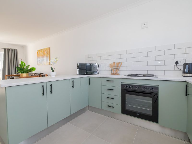 Modern kitchen featuring sage green cabinetry, white subway tile backsplash, built-in oven, gas hob, and light-toned tiled flooring.