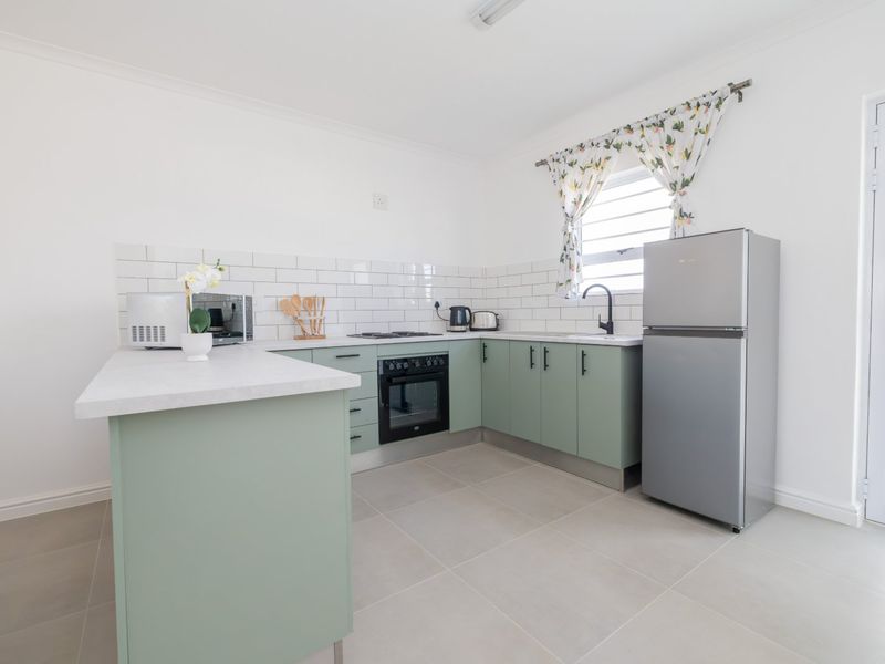 A clean, modern kitchen featuring sage green cabinetry, subway tile backsplash, built-in oven, hob, and neutral tiled flooring with direct exterior access.