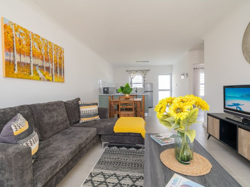 An open-plan living and kitchen area featuring neutral tiled flooring, modern cabinetry, and a functional layout connecting the lounge to the kitchen space.