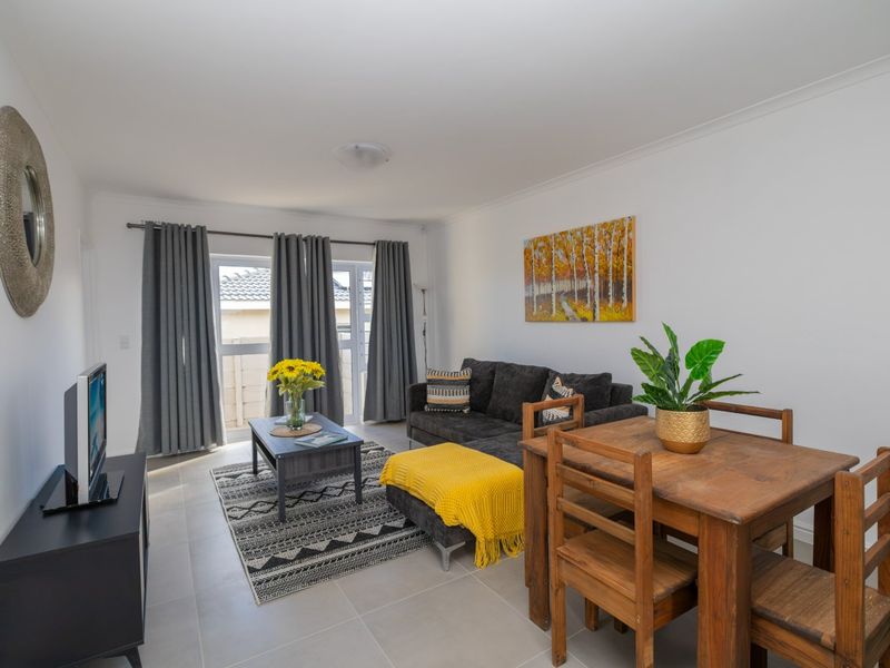 An open-plan living and dining area featuring neutral tiled flooring, clean white walls, and a sliding glass door providing access to the exterior.