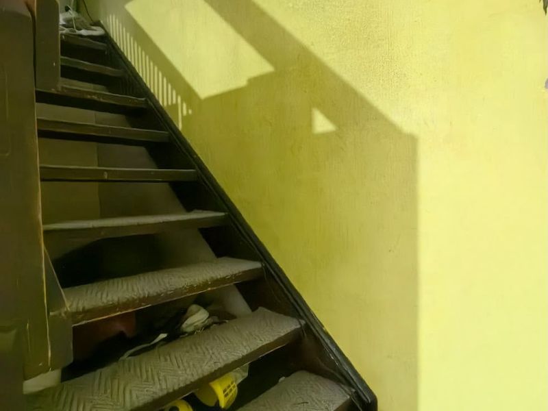 A staircase with a handrail and yellow painted walls, showing signs of wear and tear on the treads.