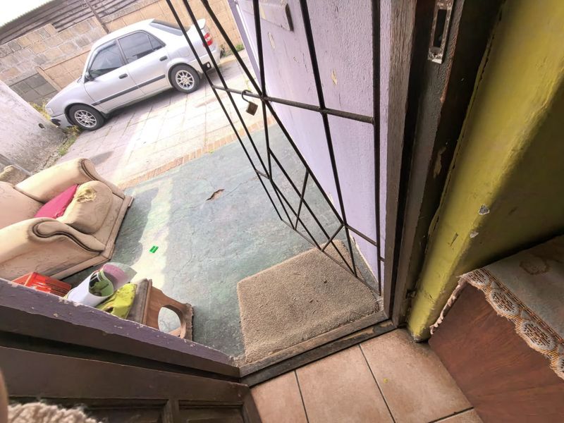 View from the entrance doorway looking out onto a concrete patio area with a security gate and tiled interior flooring.