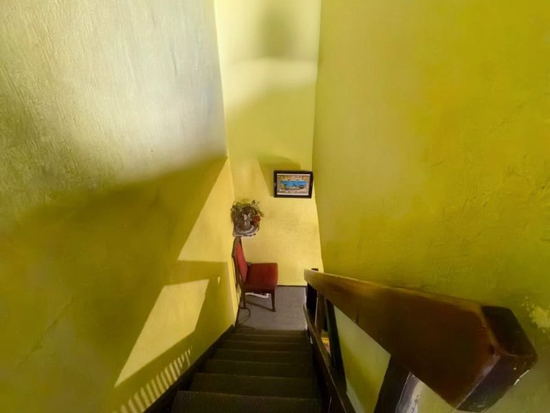 A narrow staircase featuring a wooden handrail and bright yellow wall finishes, providing access between levels of the home.