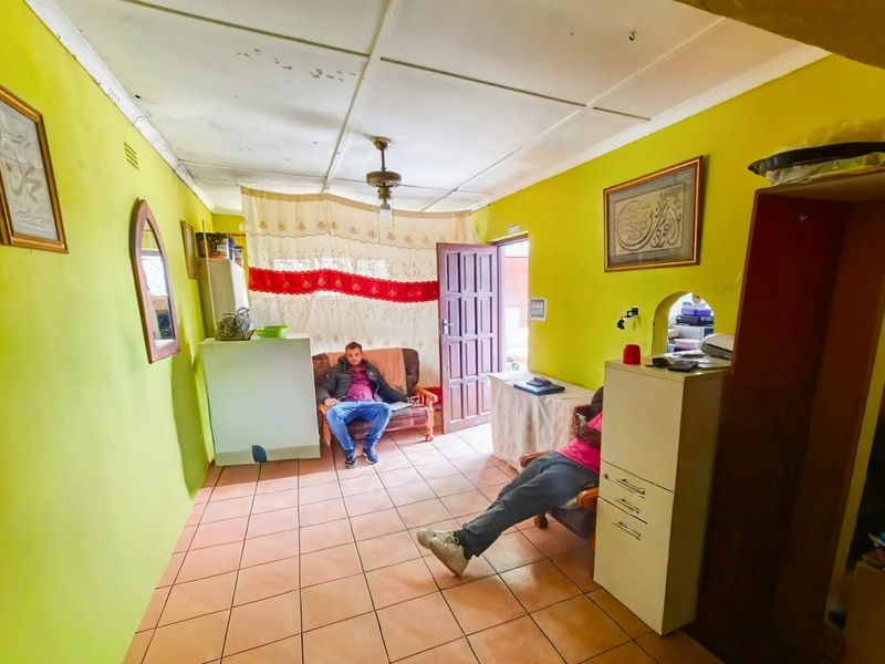 A living room featuring tiled flooring and a ceiling fan, requiring cosmetic updates to the wall finishes and ceiling tiles.
