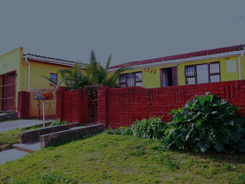 Front elevation of a single-story house featuring a yellow facade, red brick boundary wall, and security features including window bars and a metal gate.