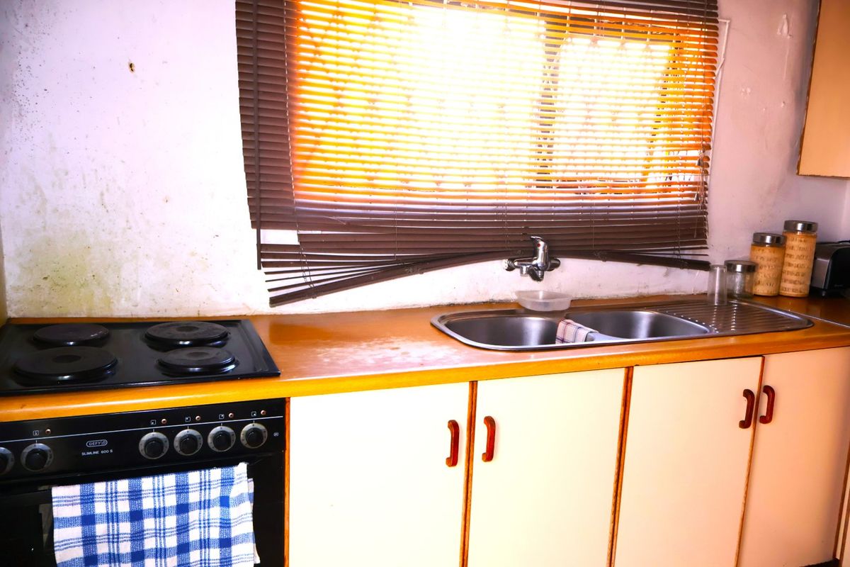 A dated kitchen featuring a built-in oven, electric hob, double bowl sink, and laminate countertops, requiring cosmetic updates and wall repairs.