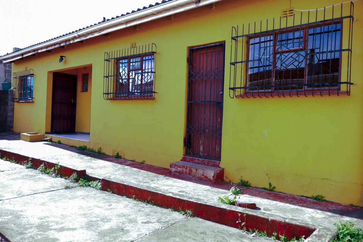 Rear exterior view of the property featuring a concrete walkway, security bars on windows, and multiple access doors.