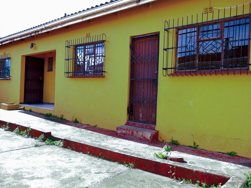 Rear exterior view of the property featuring a concrete walkway, security bars on windows, and multiple access doors.