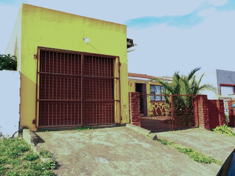 Front exterior view of the property featuring a garage with a metal security gate, concrete driveway, and brick boundary wall.