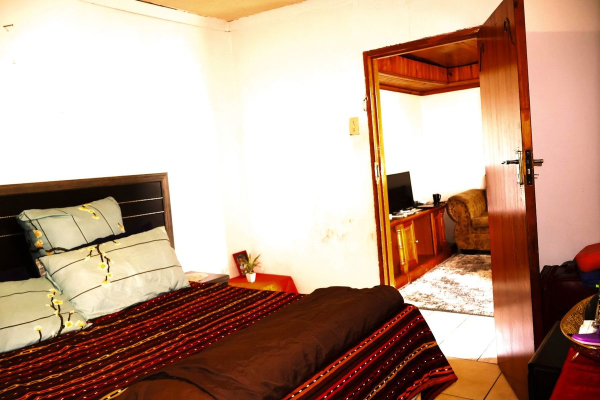 A bedroom interior featuring a doorway leading to an adjacent living space, showing signs of wall wear and dated finishes.