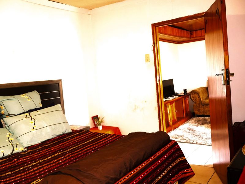 A bedroom interior featuring a doorway leading to an adjacent living space, showing signs of wall wear and dated finishes.