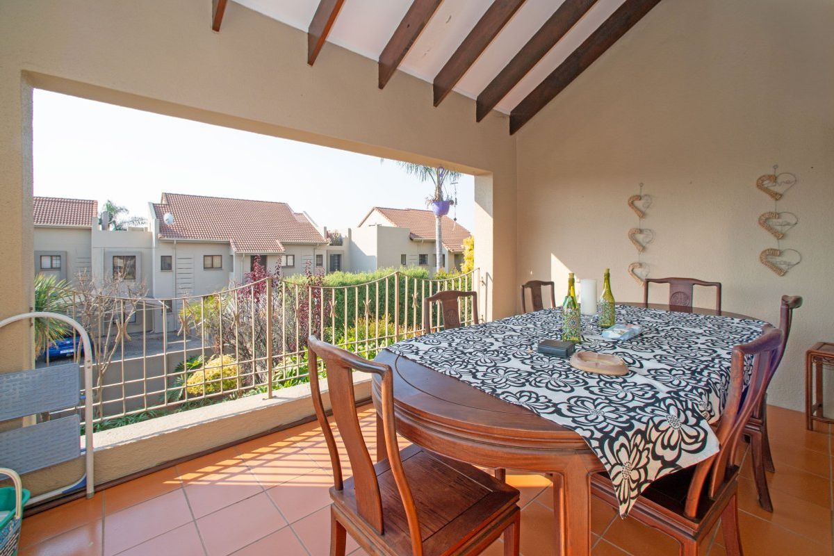 A covered balcony featuring exposed timber rafters, tiled flooring, and a metal balustrade, offering an open-air space suitable for outdoor dining.