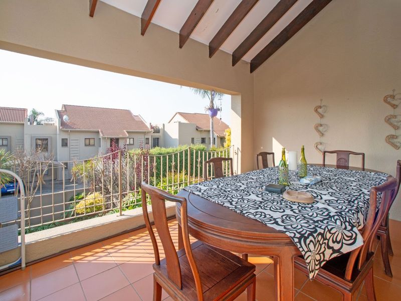 A covered balcony featuring exposed timber rafters, tiled flooring, and a metal balustrade, offering an open-air space suitable for outdoor dining.