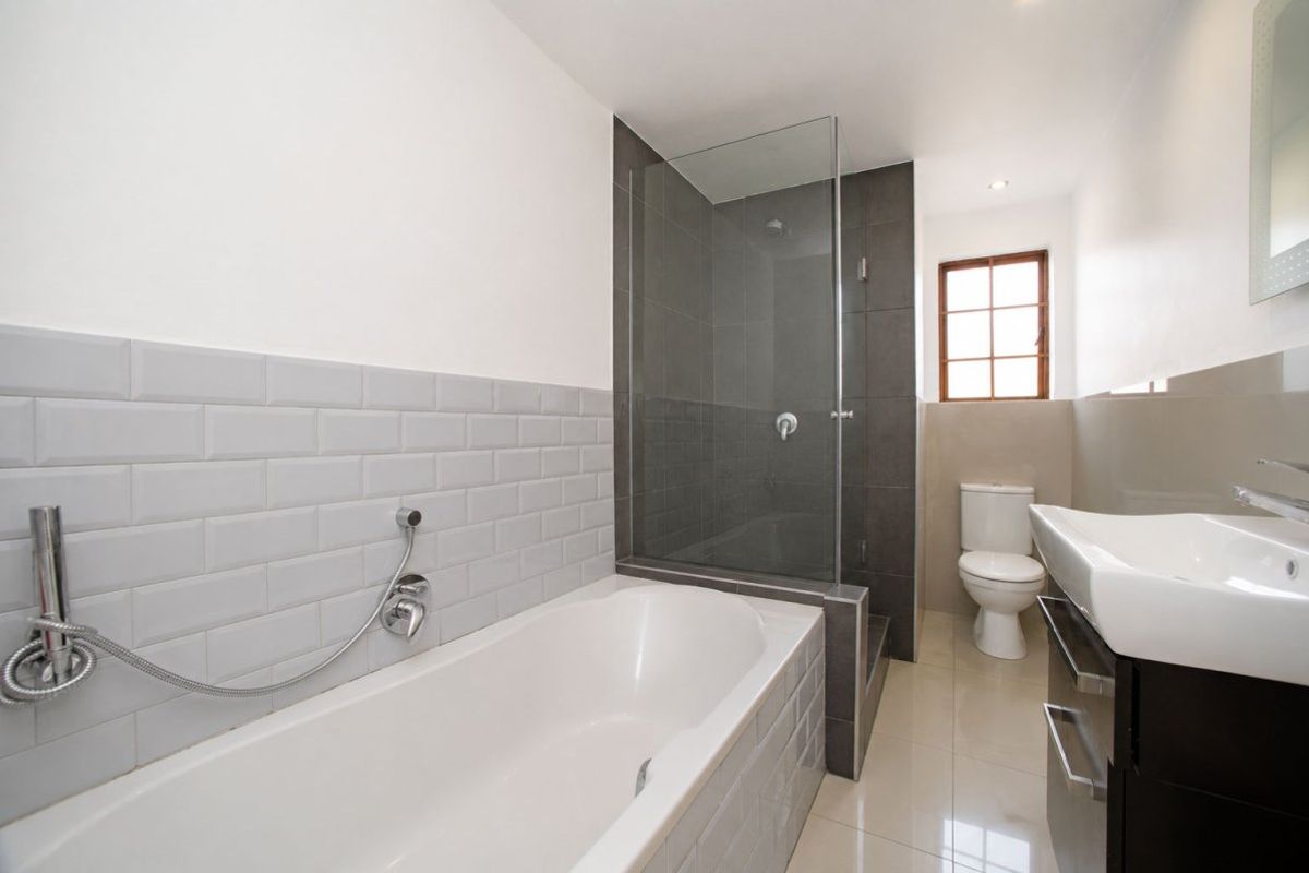 Modern bathroom featuring a bathtub, separate glass-enclosed shower, vanity basin, and toilet with neutral subway tile accents and tiled flooring.