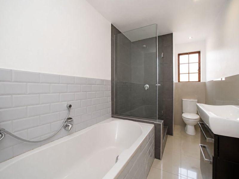 Modern bathroom featuring a bathtub, separate glass-enclosed shower, vanity basin, and toilet with neutral subway tile accents and tiled flooring.