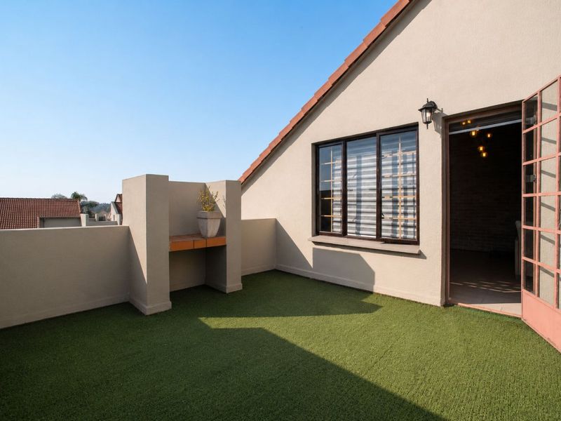 A private balcony featuring artificial grass, a built-in braai area, and direct access to the interior through a metal security gate.