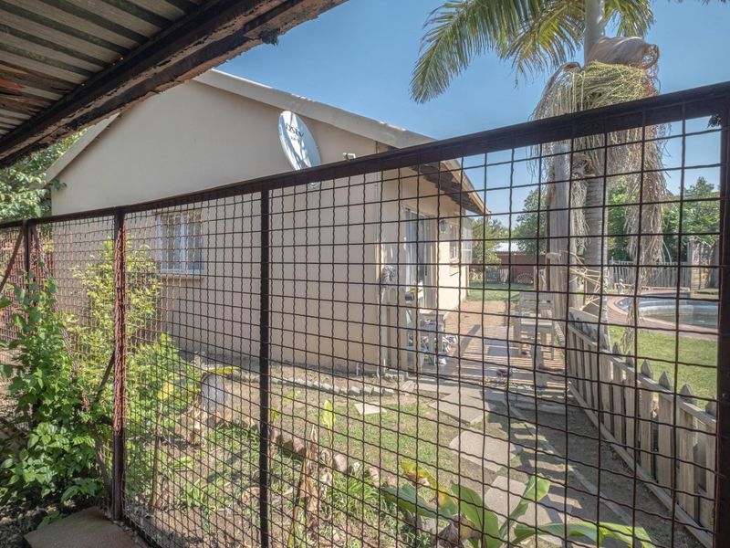 Rear exterior view of the property featuring a garden area, swimming pool, and wire mesh fencing with a corrugated metal roof structure.