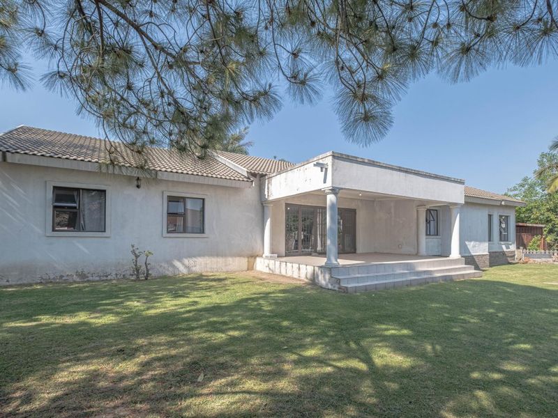 Rear view of the house featuring a covered patio with concrete columns, tiled roof, and a spacious lawn area.