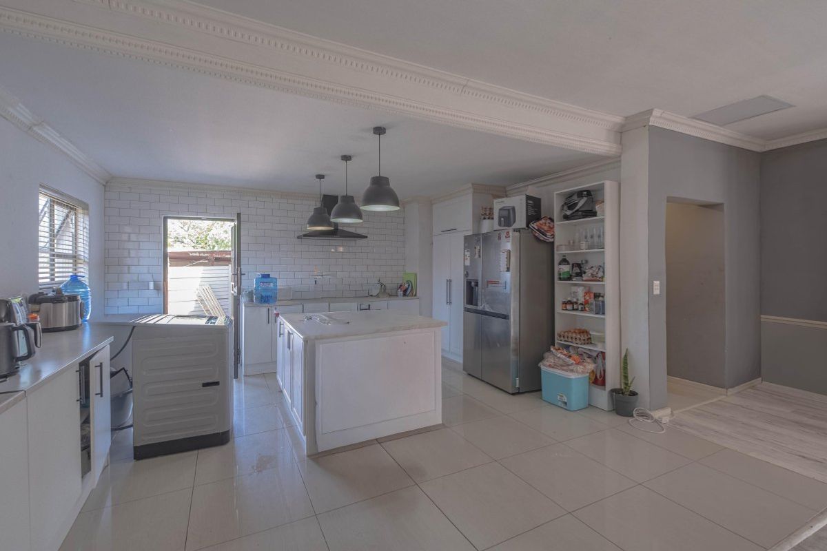 Spacious kitchen featuring a central island, subway tile backsplash, modern pendant lighting, and ample built-in cabinetry with tiled flooring throughout.