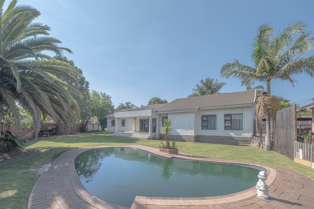 Rear view of the property featuring a swimming pool, a covered patio area, and a spacious garden with established trees.