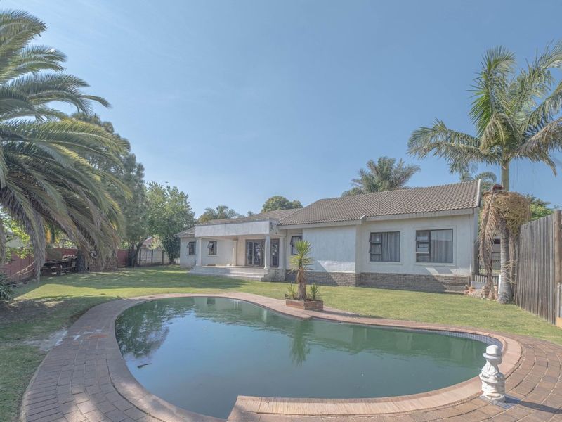 Rear view of the property featuring a swimming pool, a covered patio area, and a spacious garden with established trees.