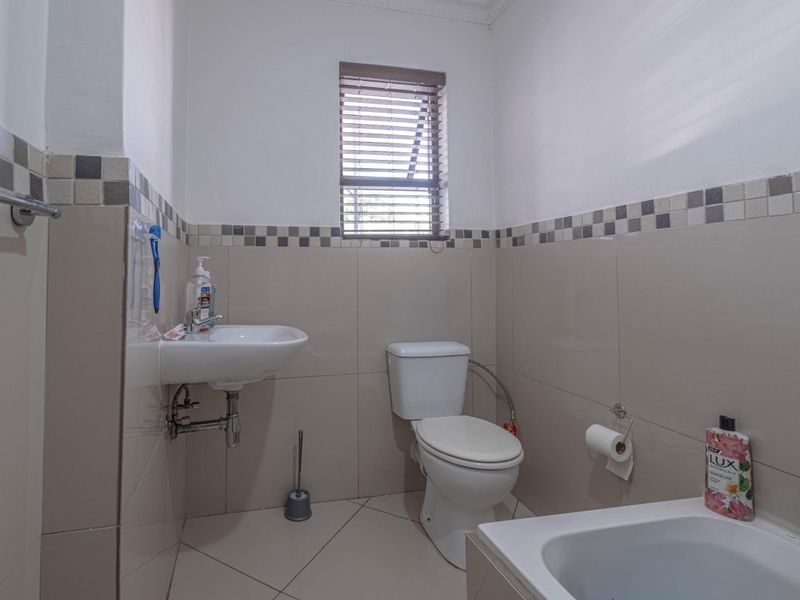 A functional bathroom featuring a wall-mounted basin, toilet, and bathtub with neutral wall and floor tiling.