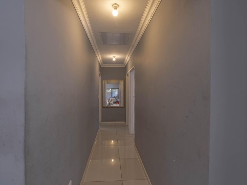 A neutral-toned hallway featuring tiled flooring, ceiling cornicing, and an access hatch, providing a clean transition between living spaces.