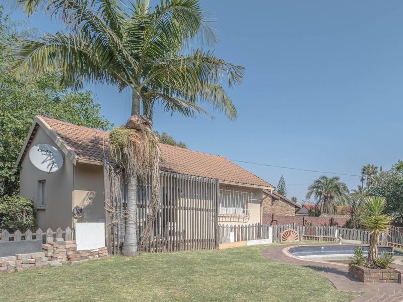 Rear exterior view of the house featuring a swimming pool, paved surround, timber privacy screening, and a large palm tree in the garden.