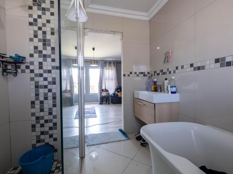 A bathroom featuring a freestanding bathtub, vanity basin, and glass shower enclosure with decorative mosaic tile accents and unfinished doorway trim.