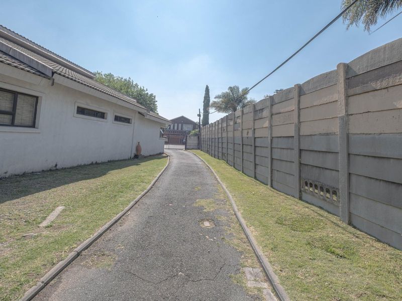 A side driveway approach featuring an asphalt path, precast concrete boundary wall, and access to the property entrance.