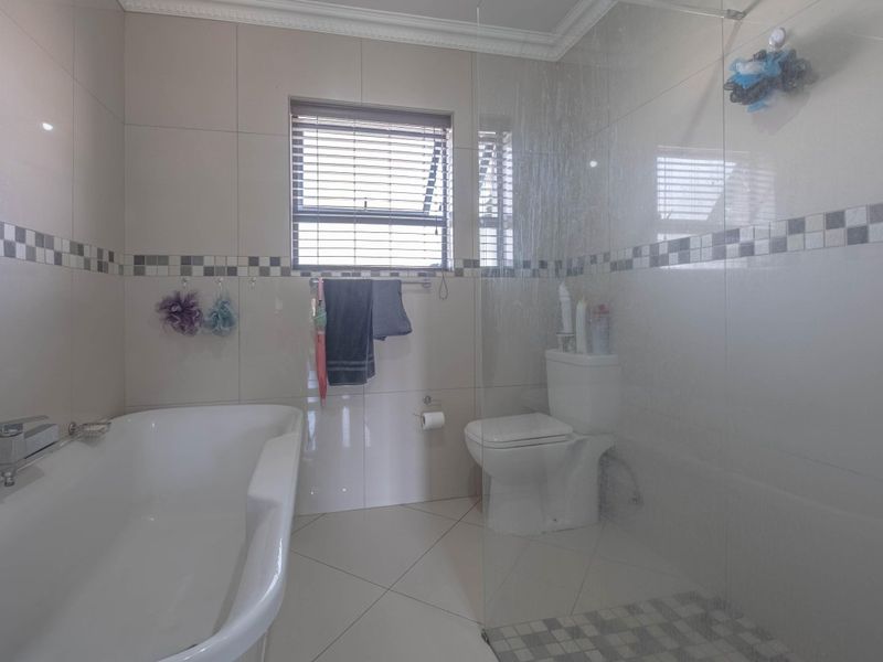 A well-maintained bathroom featuring a bathtub, a glass-enclosed shower, and neutral wall and floor tiling.