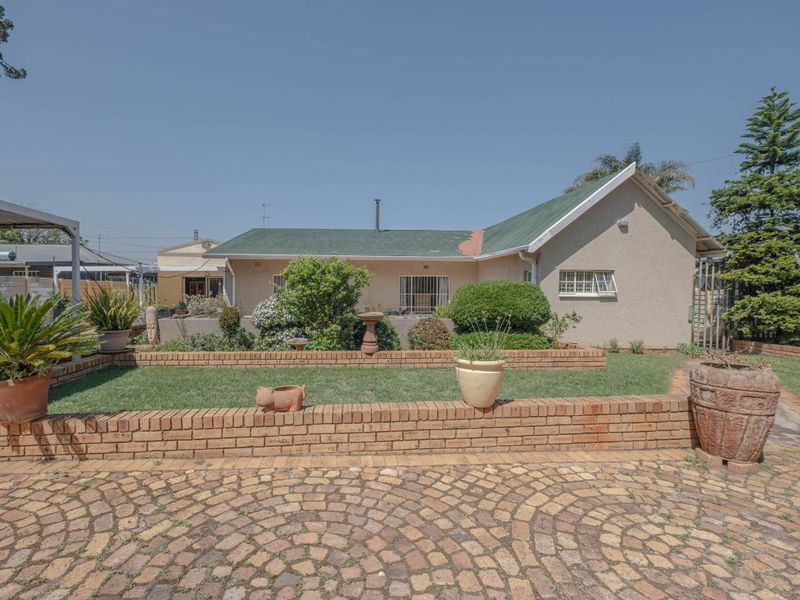 Rear view of the house featuring a landscaped garden with brick retaining walls, cobblestone paving, and a metal roof.