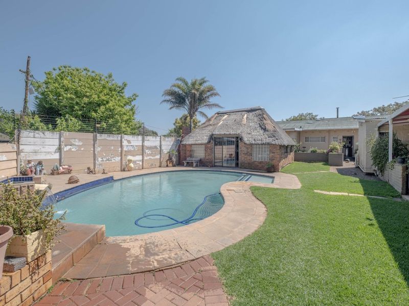 Outdoor pool area featuring a swimming pool, lawn, brick paving, and a traditional thatched lapa structure in the rear garden.
