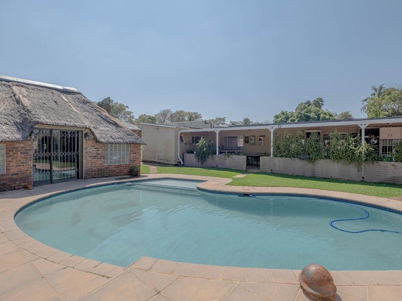Outdoor pool area featuring a swimming pool, paved deck, and a covered patio attached to a brick building with a traditional thatched roof.