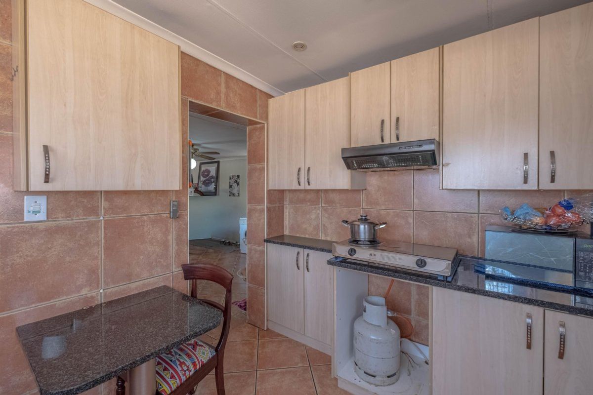 Compact kitchen featuring laminate cabinetry, granite countertops, and ceramic tiling, with an integrated extractor fan and gas hob setup.