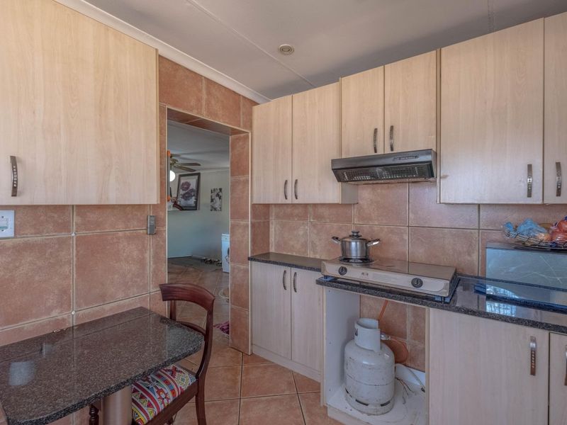 Compact kitchen featuring laminate cabinetry, granite countertops, and ceramic tiling, with an integrated extractor fan and gas hob setup.