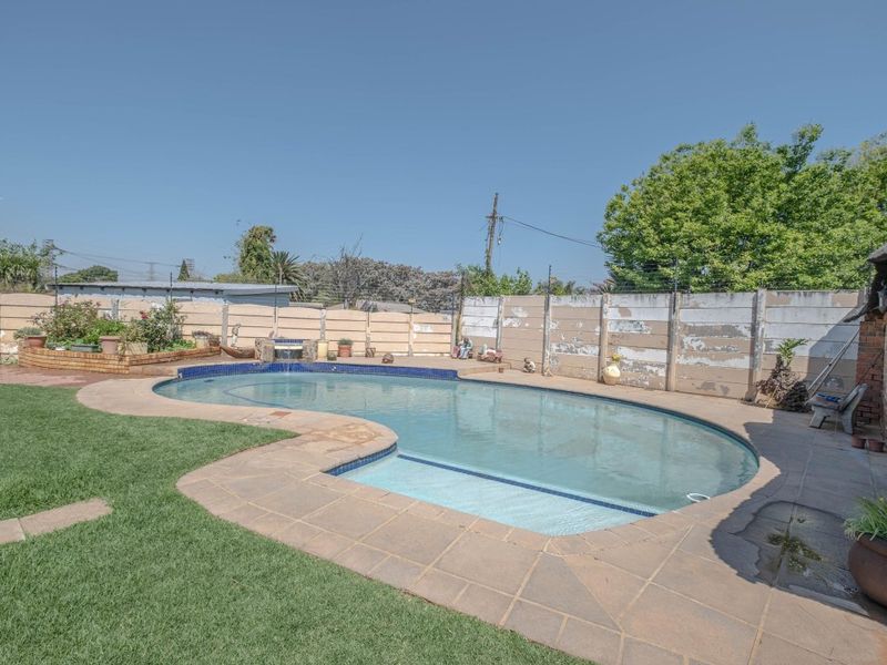 Outdoor pool area featuring a curved swimming pool with paved surround, a raised brick planter, and a perimeter boundary wall.