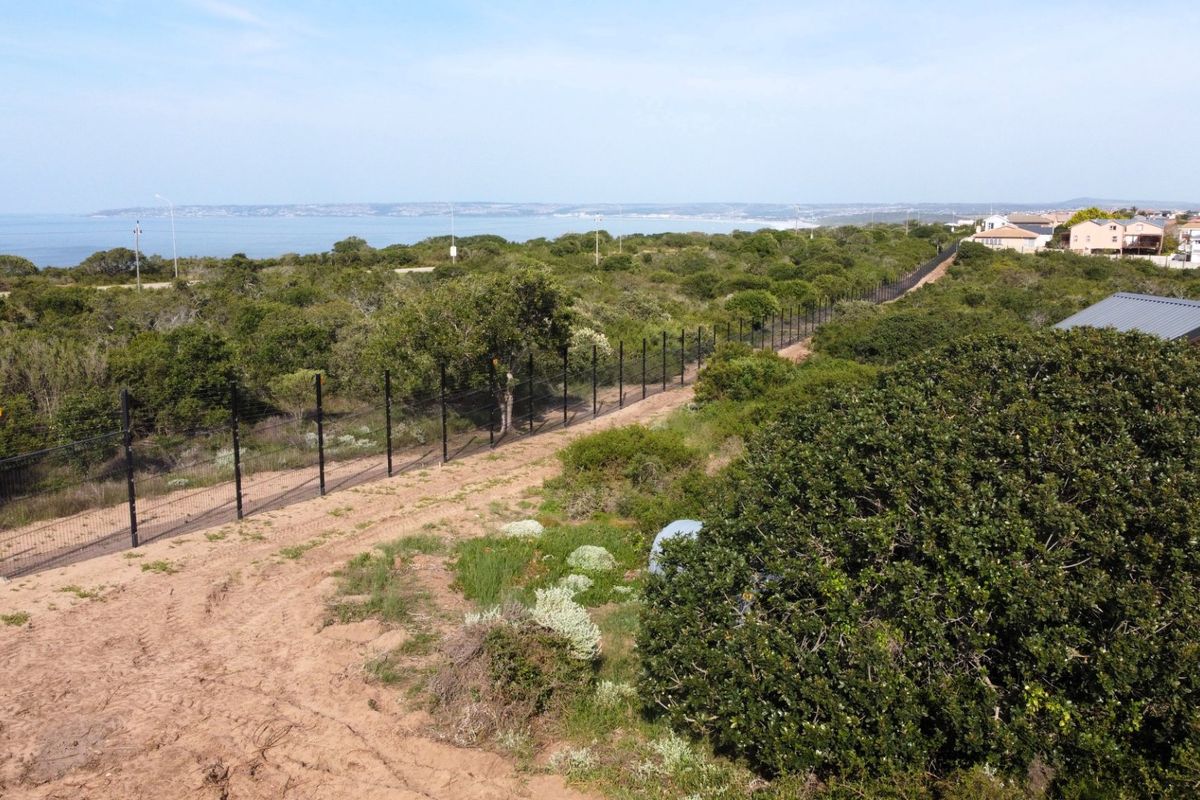 Aerial view of a vacant residential plot featuring perimeter fencing and natural coastal vegetation with distant ocean views.